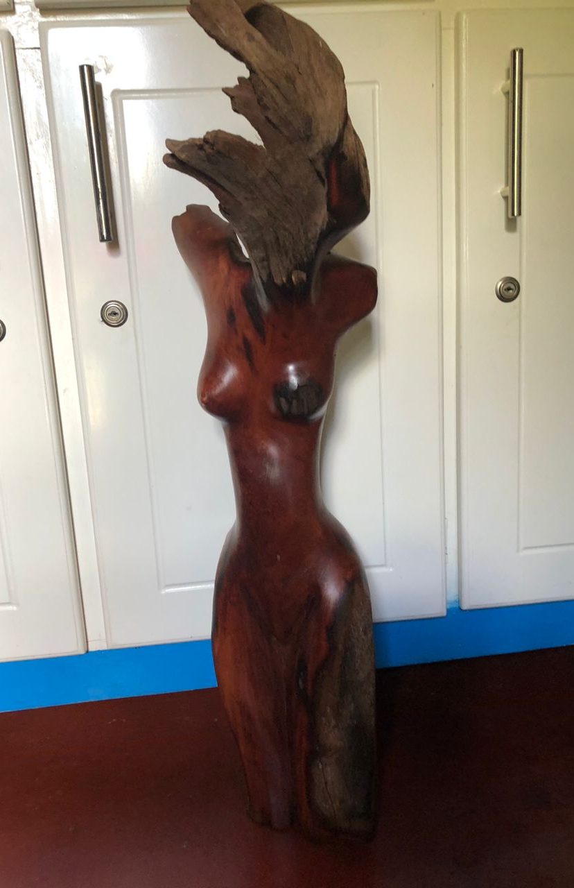 Artistic wooden sculpture of a stylized female figure, featuring smooth brown contours and abstract wood elements representing hair.