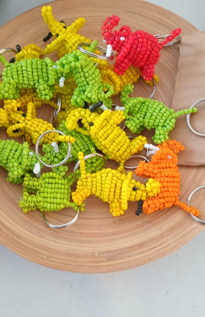 A wooden bowl filled with vibrant beaded keychains shaped like small animals, featuring dinosaur designs in green, yellow, and red colors.