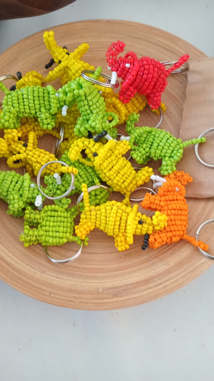 A wooden bowl filled with vibrant beaded keychains shaped like small animals, featuring dinosaur designs in green, yellow, and red colors.