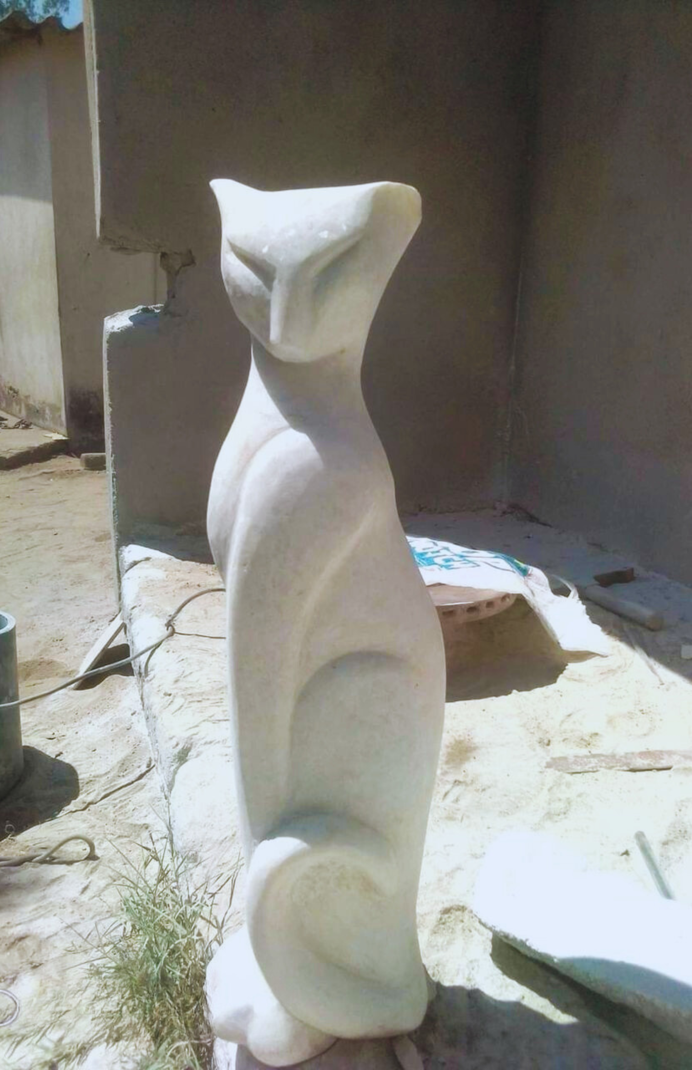 Tall and elegant white stone sculpture of a cat displayed outdoors, highlighting smooth curves and modern design in an artistic workspace.