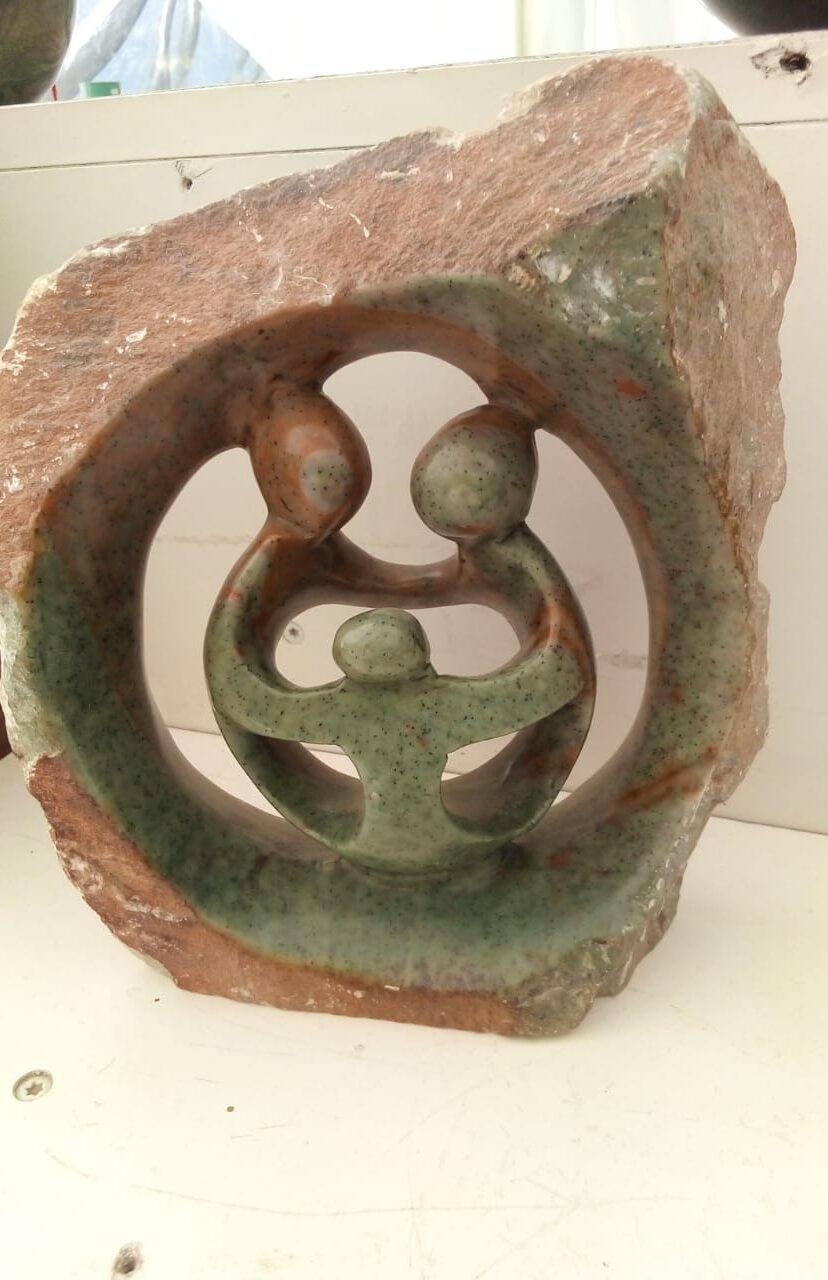 A decorative stone sculpture featuring a circular design with two abstract figures embracing a smaller figure in the center. This portrays significant family bonds