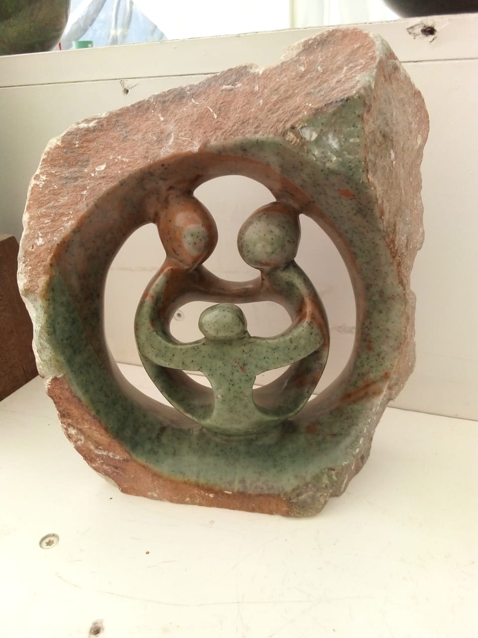 A decorative stone sculpture featuring a circular design with two abstract figures embracing a smaller figure in the center. This portrays significant family bonds